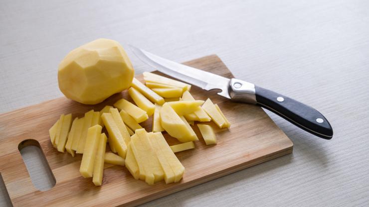 Fresh potatoes, peeled, for cooking French fries. Knife and vegetables, root vegetables on a cutting board, on the kitchen table at home, in a restaurant or cafe. The concept of cooking, home life. Vegetarian or vegan life. Cooking lessons.